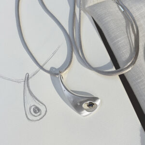 Outback Fossil Pendant in silver with sapphire set in 18ct yellow gold and diamonds, resting on a design sketch. Sculptural pendant inspired by the Australian outback, highlighting its organic form and refined craftsmanship.