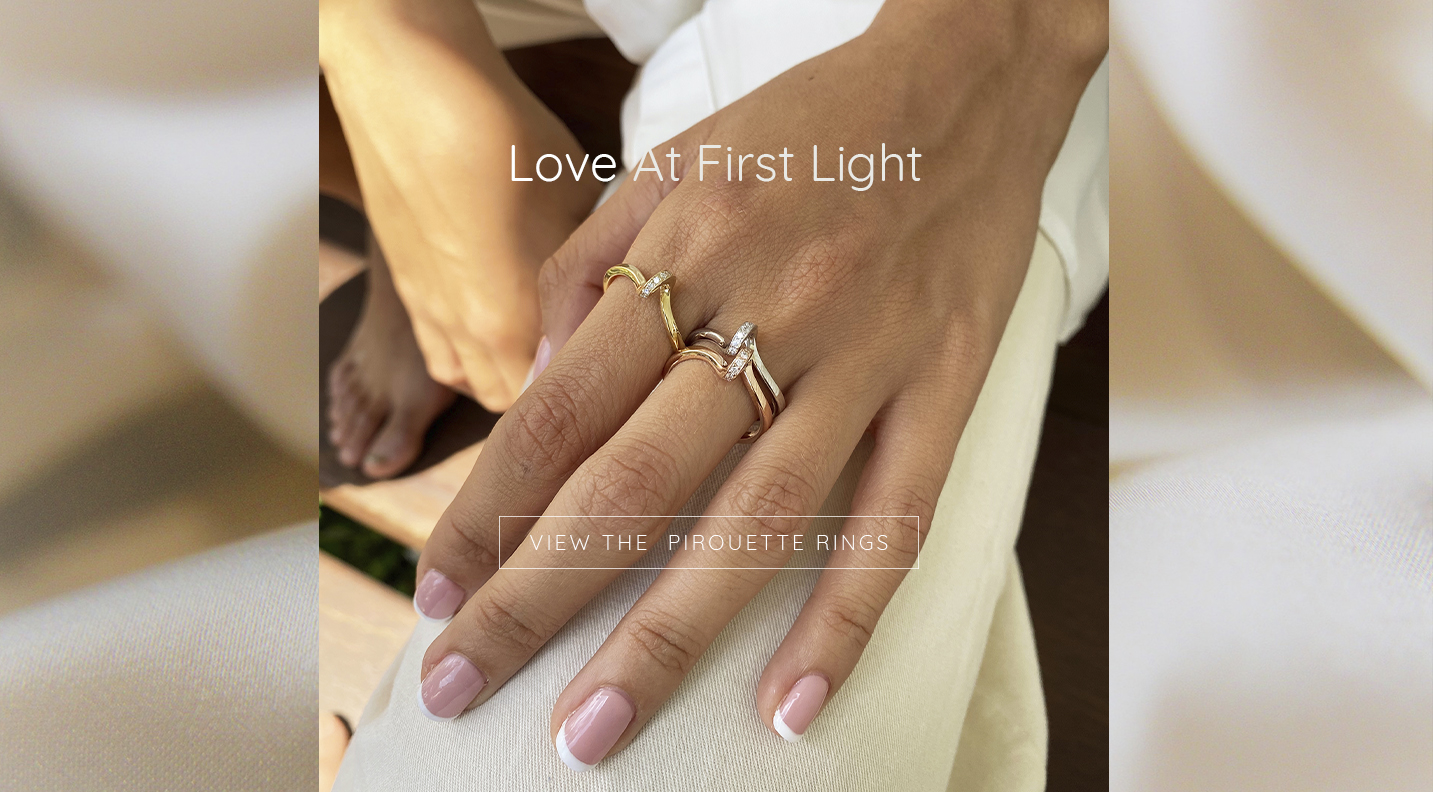 Pirouette diamond rings in yellow, white, and rose gold worn on hand resting on white trousers, morning sunlight and silk doona covers in background