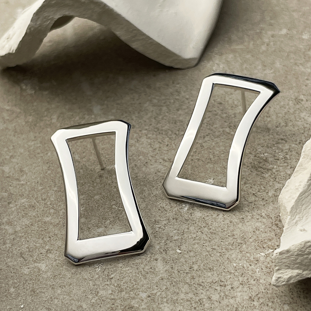 Deanna Earrings in polished sterling silver, resting on a natural stone background. Simple, refined design inspired by Greek architecture, highlighting the smooth polished finish.